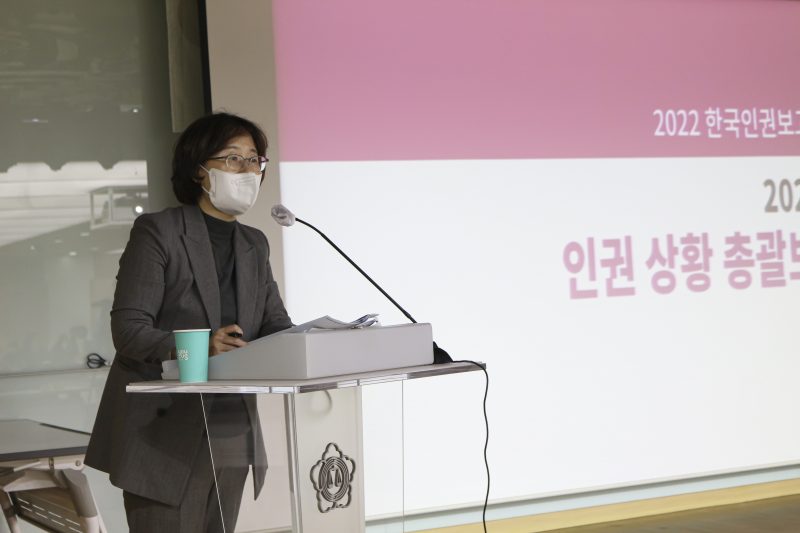 인권상황 총괄보고 PPT 화면 앞 마이크가 있는 연단에 서서 발표하는 이상희 준비위원장